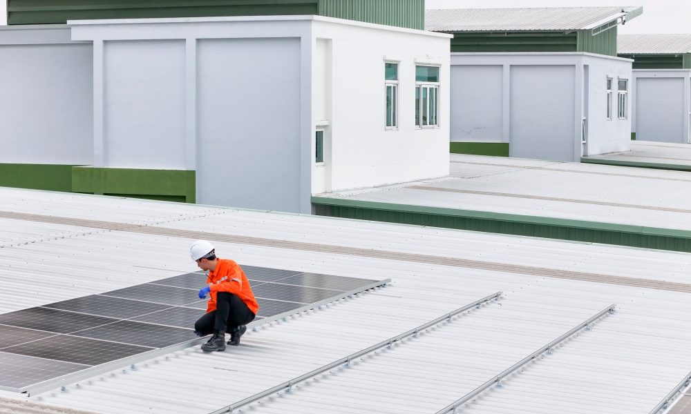 Aerial view of a rooftop with solar panels, showing a technician in safety performing maintenance.