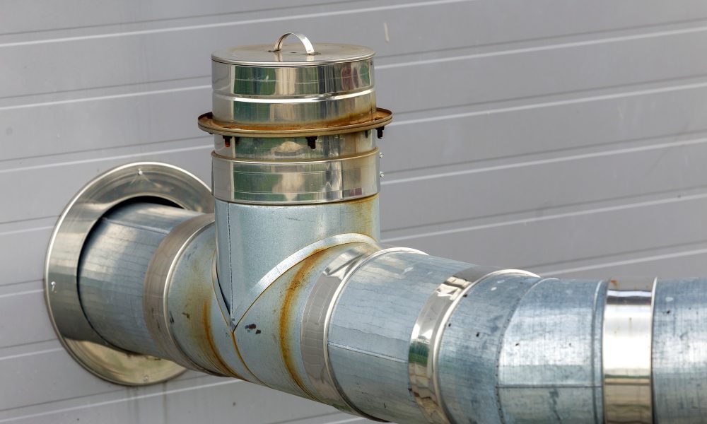 Metallic exhaust smoke pipes installed on house exterior wall.