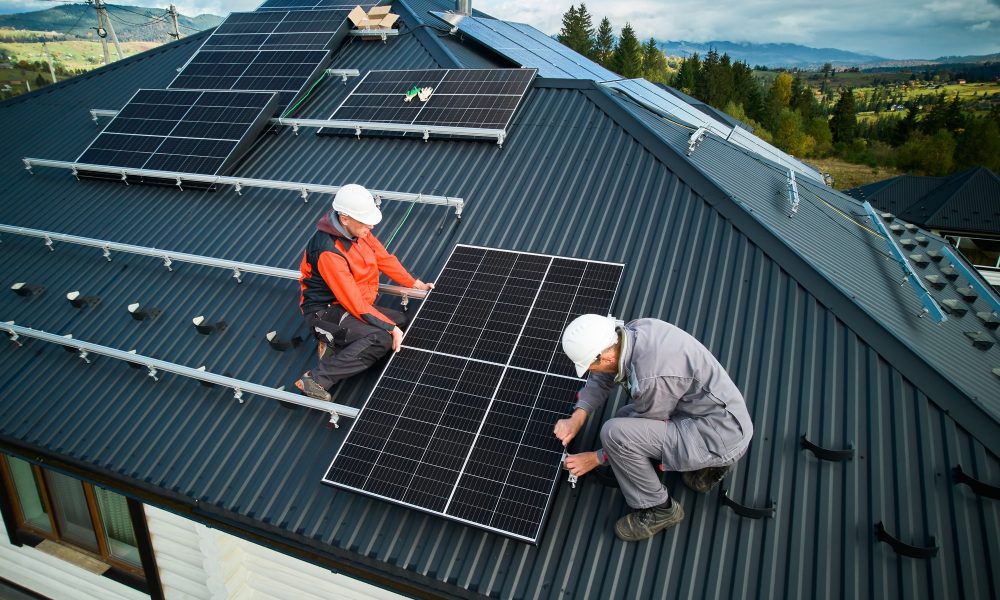 Technicians installing photovoltaic solar panels on roof of house.